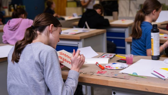 Schülerinnen und Schüler arbeiten in einem Klassenzimmer an kreativen Projekten, mit Bastelmaterialien wie Farben, Pinseln und Papier auf den Tischen." Schülerinnen und Schüler arbeiten in einem Klassenzimmer an kreativen Projekten, mit Bastelmaterialien wie Farben, Pinseln und Papier auf den Tischen."
