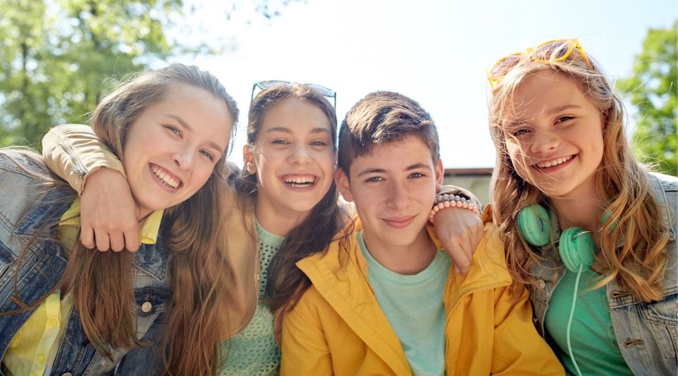 Vier lachende Kinder stehen eng beieinander im Freien und legen sich freundschaftlich die Arme um die Schultern.